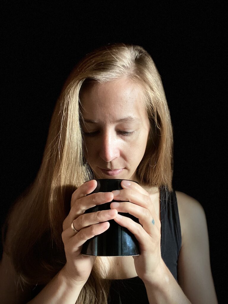 Eine blonde Frau vor einem schwarzen Hintergrund mit einer schwarzen Tasse in der Hand