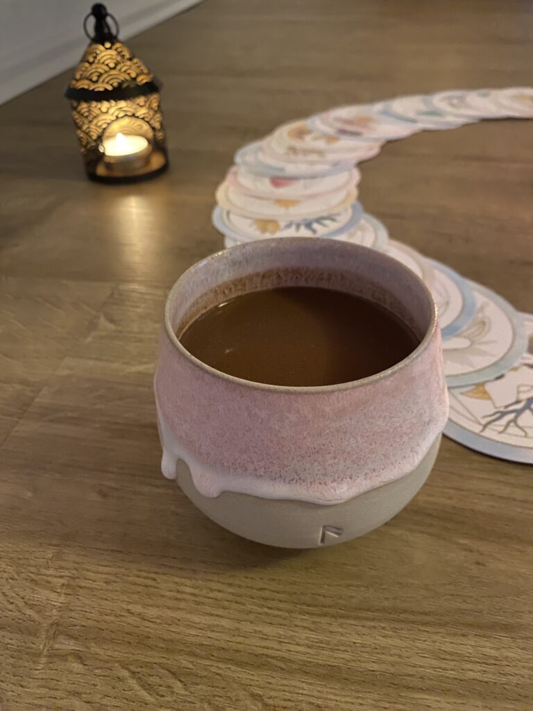 Ein Keramikbecher mit Cacao steht vor einem Kartenset. Im Hintergrund ist links ein Teelichthalter im orientalischen Stil