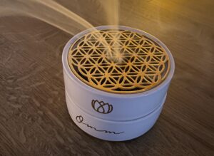 Eine weiße Räucherschale mit goldenem Sieb steht auf einem Holzboden. Reinigender Rauch steigt in der Mitte empor. Das Bild dient als Titelbild für den Beitrag energetisches Räuchern Anleitung