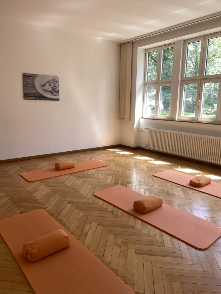 Ein lichtdurchfluteter Raum mit orangenen Yogamatten und Meditationskissen